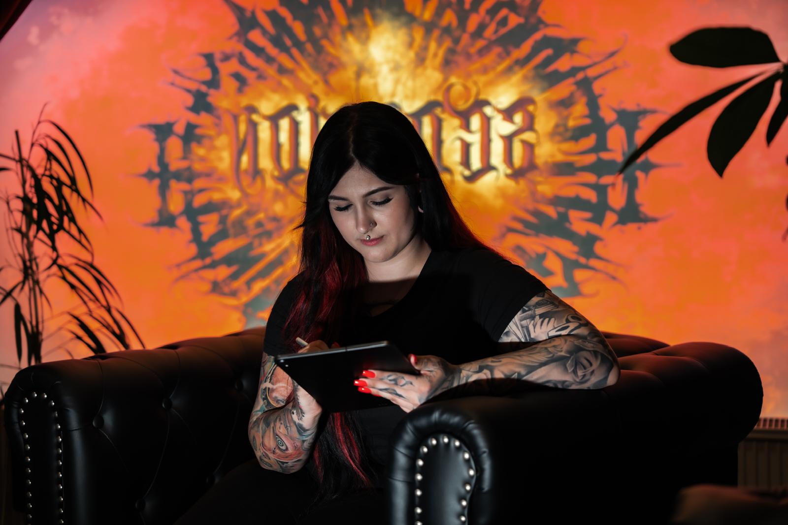 Lisa im Scorpion Ink Tattoo Studio in Bautzen — am Tablet, dunkler Sessel, Dark-Art-Motiv im Hintergrund.