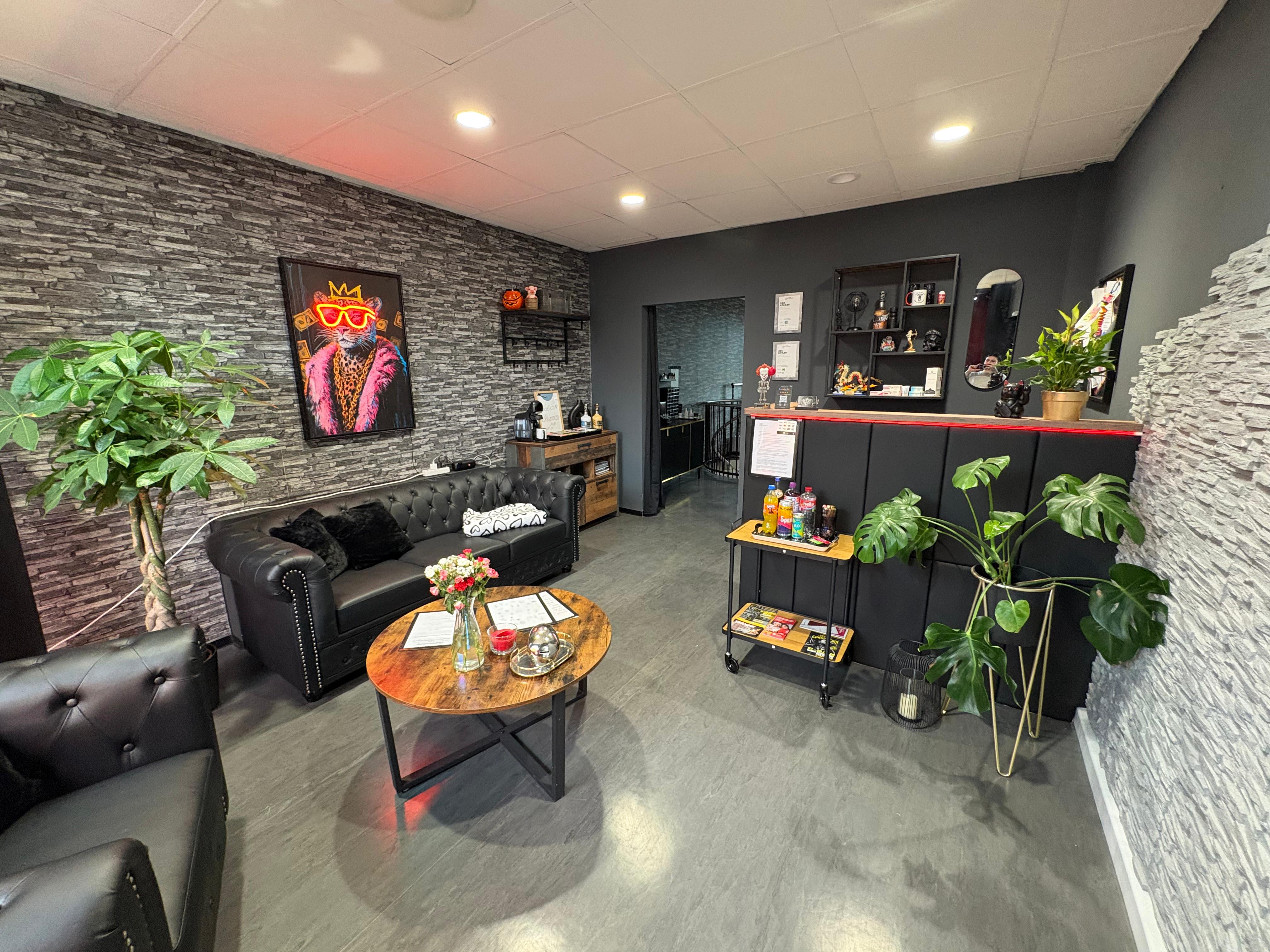 Empfangs- und Loungebereich des Scorpion Ink Tattoo Studios in Bautzen — Chesterfield-Ledersofas, Steinwand, warmes Licht.